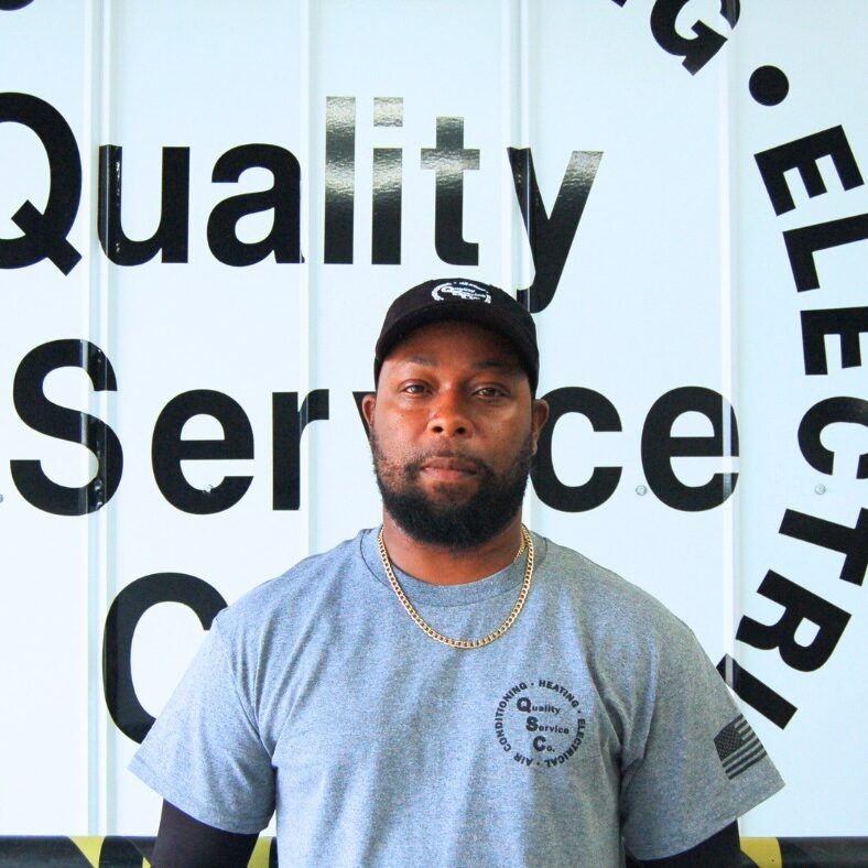 Man in gray shirt and cap standing in front of a sign reading Quality Service.