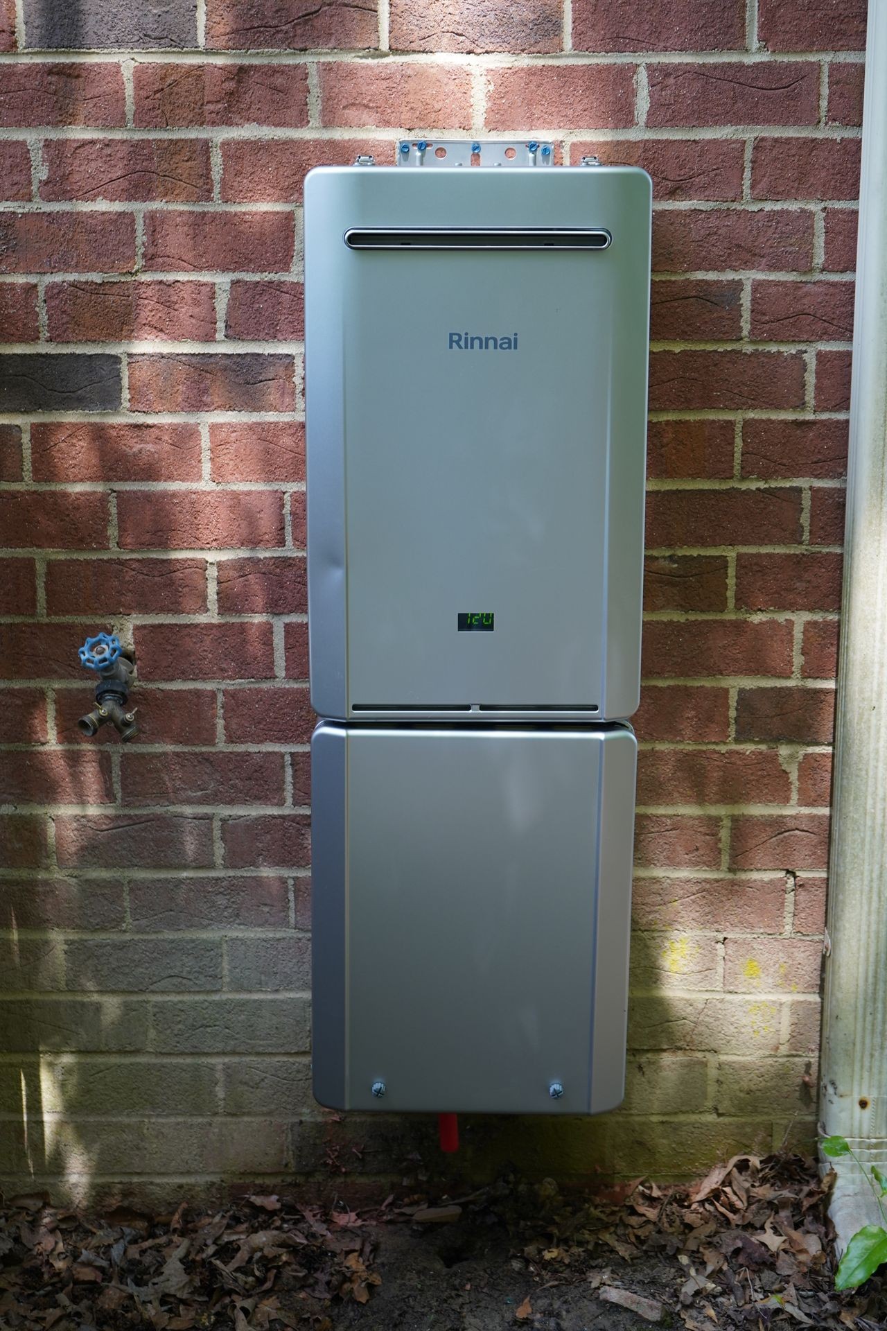 Outdoor tankless water heater mounted on a brick wall, with a hose bibb nearby.