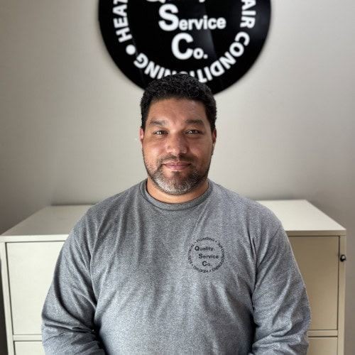 Man in gray shirt sitting in front of a company sign on the wall.