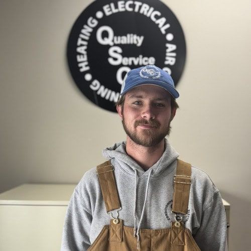 Man in a hoodie and cap standing in front of a sign for a heating and electrical service.