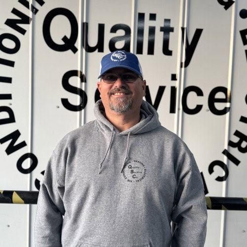 Person in a gray hoodie and blue cap smiling in front of a wall with text.