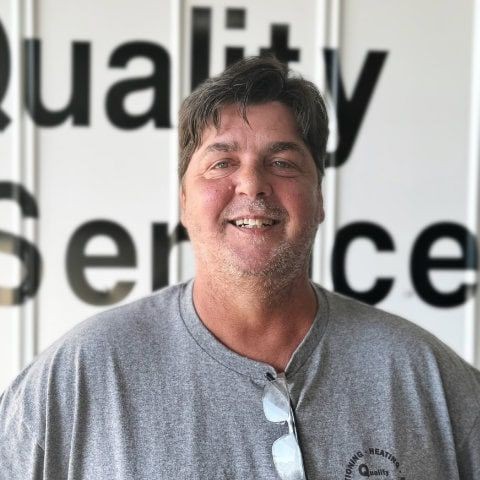 Man smiling in front of a wall with 'Quality Service' partially visible in the background.