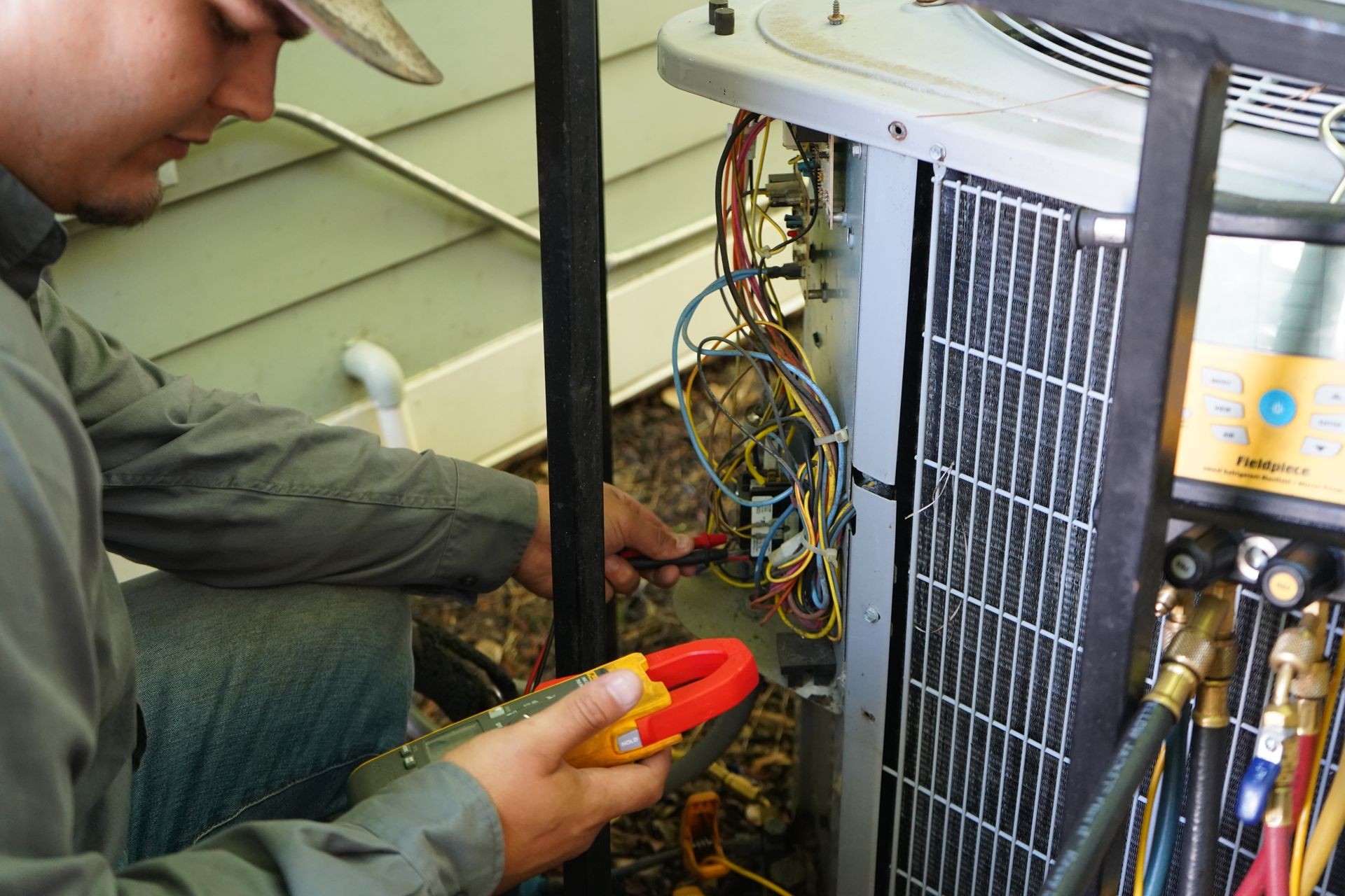 Technician performing a voltage check on an outdoor air conditioning unit using a digital multimeter.