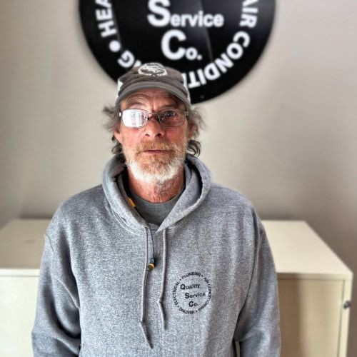 Man in glasses wearing a gray hoodie and cap with a service company logo in the background.