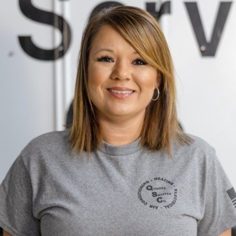 Woman in a gray t-shirt standing in front of a large sign with partial text visible.