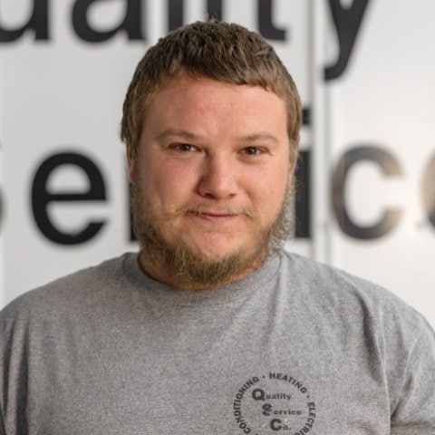 Man in a gray shirt standing in front of a partially visible sign with large letters.