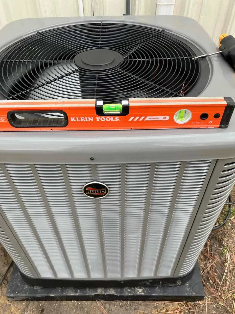 An orange spirit level rests on a Ruud outdoor condenser.