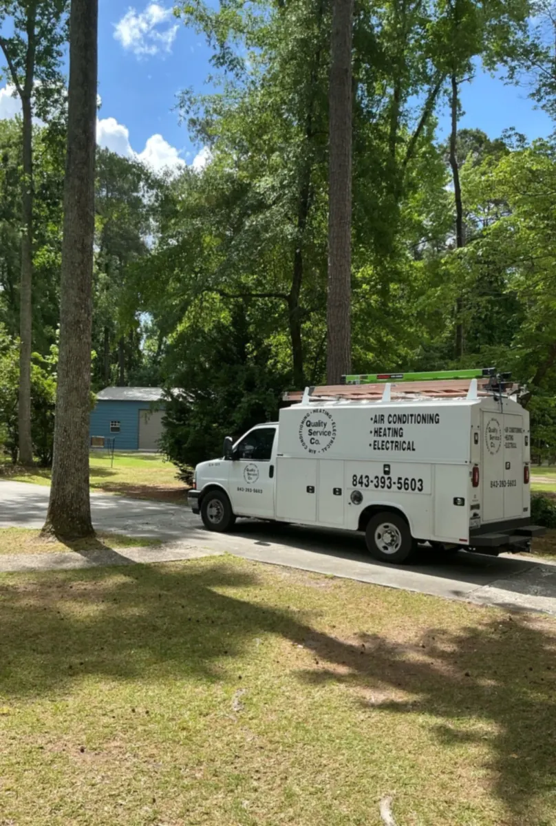 A QSC service truck is parked on a wooded residential driveway.