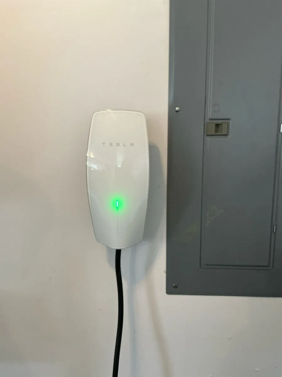 A Tesla wall connector is mounted beside an electrical panel.