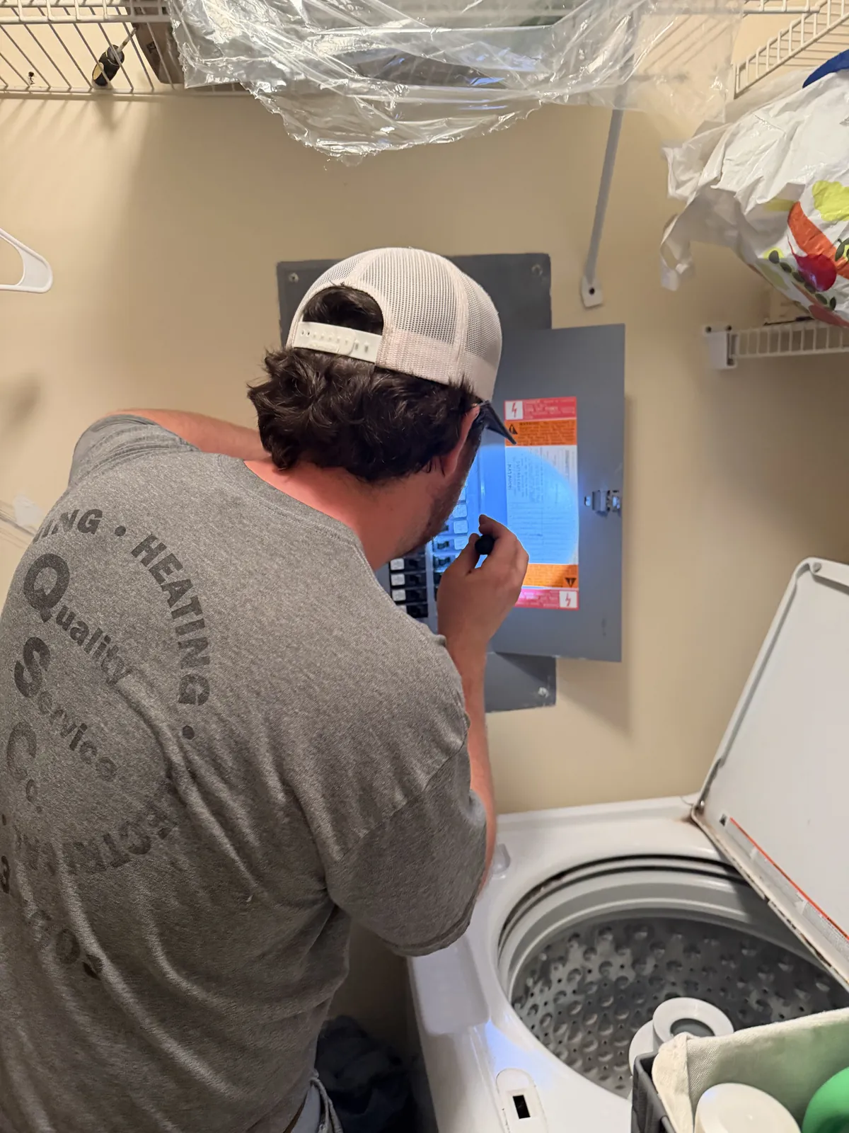 A technician in a Quality Service Company shirt examines an open electrical panel.