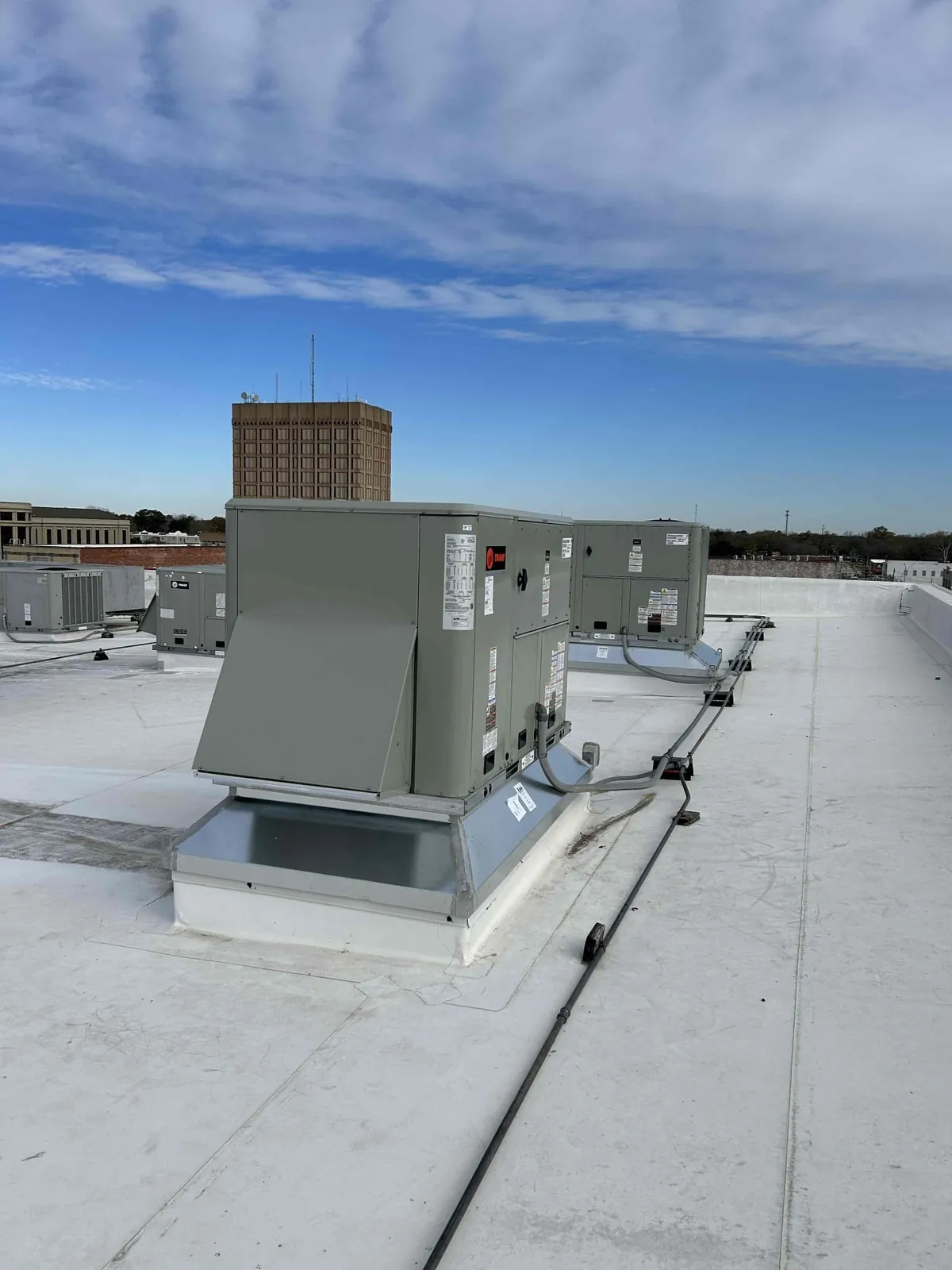 Several HVAC units stand on a flat white roof.