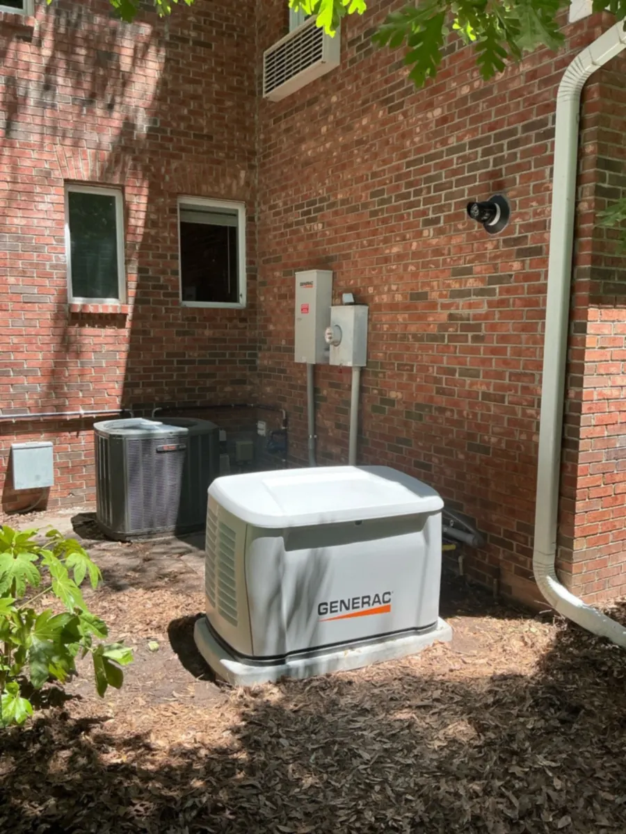 A Generac standby generator sits beside a brick house.