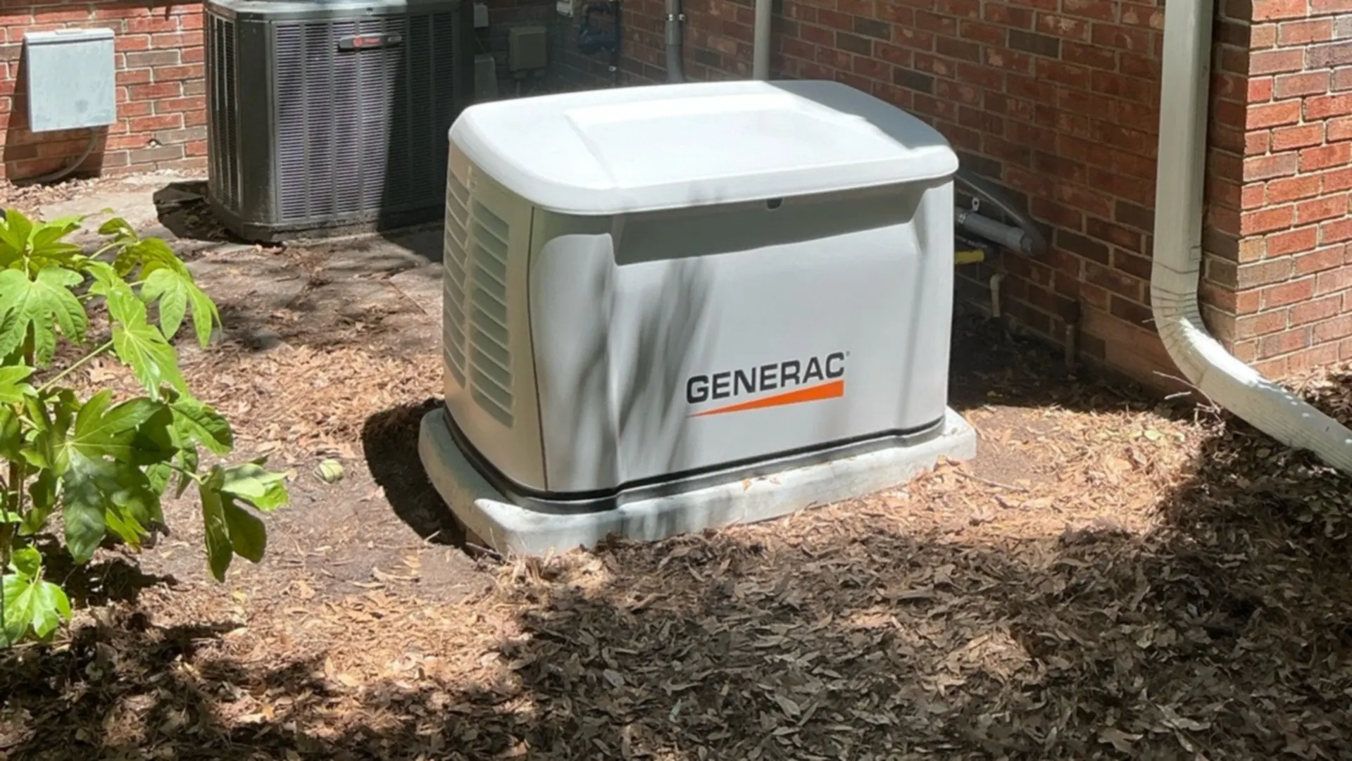 A Generac standby generator sits beside a brick house.