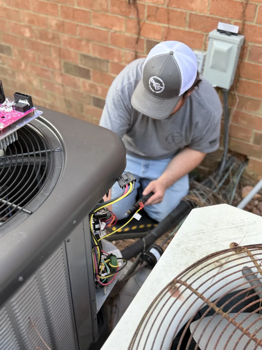 A technician works on wiring inside an outdoor condenser.