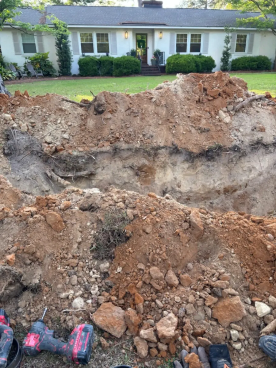An open trench and piles of soil cross a residential lawn.