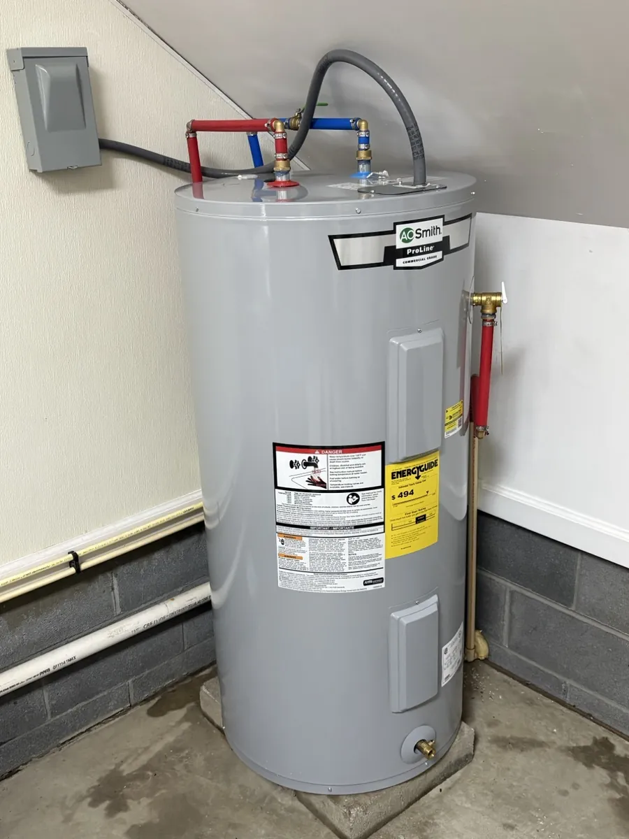 A tank water heater stands beside connected red and blue pipes.